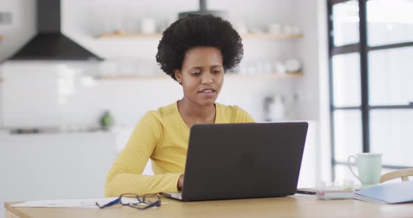 Happy african american woman sitting at table using laptop