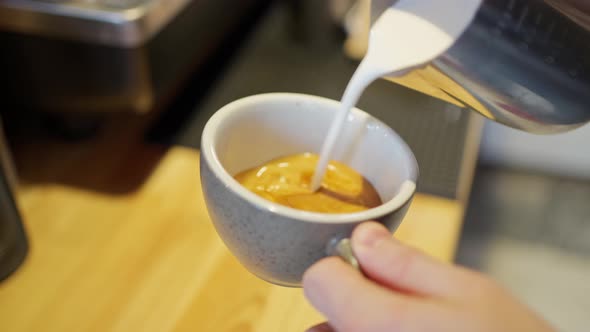 Barista's Hands Pour Frothed Milk From the Pitcher Into Freshly Brewed Espresso Coffee and Draw on