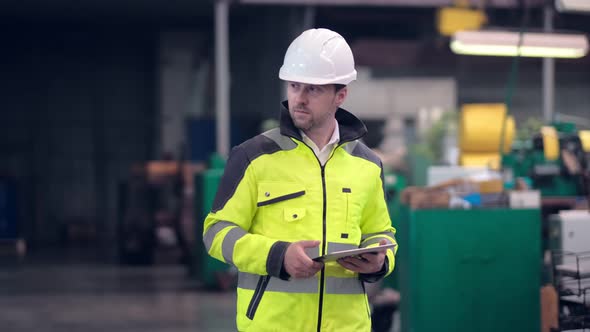 Engineer in Hard Hat is Moving Through a Heavy Industry Factory with a Tablet Computer