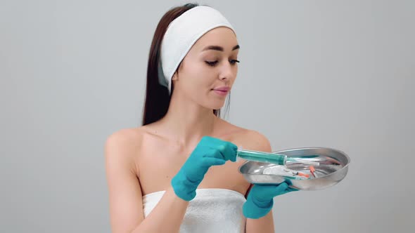 Portrait of a young beautiful woman in medical gloves choosing syringes from medical kidney dish.