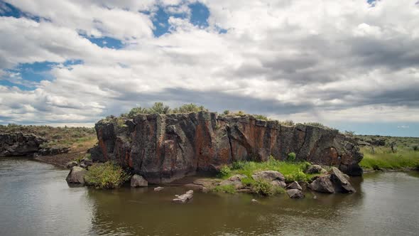 Time lapse of thick clouds moving over colorful rock along river