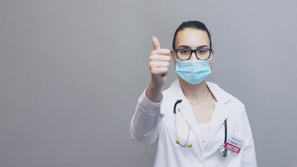 Young Female Doctor in Uniform Glasses Facial Mask Showing Thumb Up Sign