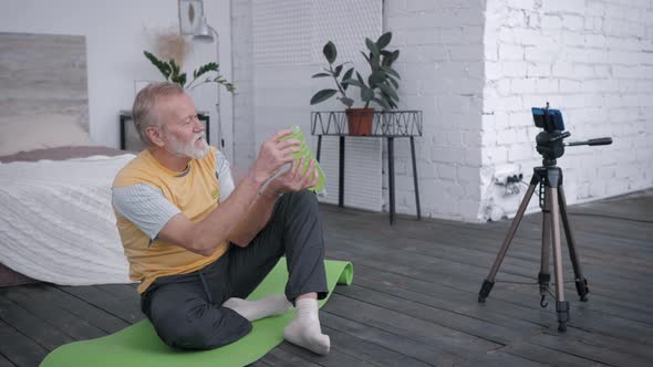 Influential Elderly Male Blogger Records Video Review of Vitamin Water for Blog on a Smartphone