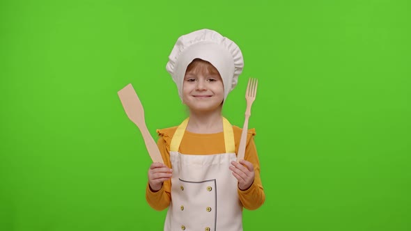 Child Girl Kid Dressed As Cook Chef Showing Wooden Fork and Spatula Smiling Nods Head in Agreement