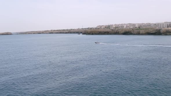 Aerial footage flying towards a boat speeding in the sea in front of the cliffs of Polignano a Mare,