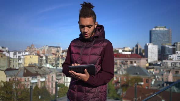 Thoughtful Positive African American Man Scrolling Social Media in App on Tablet Looking Away