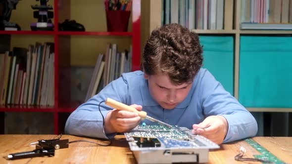 Caucasian Child solders printed circuit board with soldering iron.
