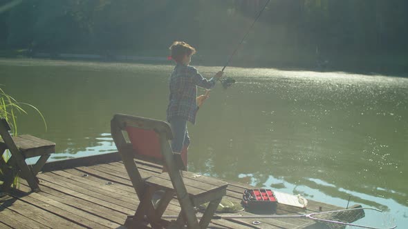 Positive Preadolescent Arab Boy with Spin Fishing Rod Fishing on Lake at Sunrise