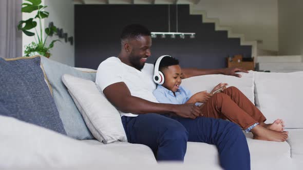 African american father and son using a digital tablet together with boy wearing headphones