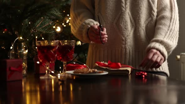 Woman in sweater is wrapping a Christmas gift on a table
