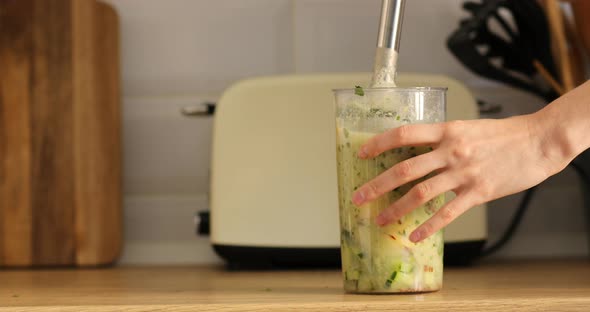 cropped photo of hand of young woman making healthy smoothie juice with fruits and herbs with blende