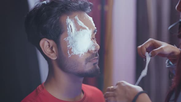 Make up artist putting prosthetic insert in white color on man's face to make Halloween mask