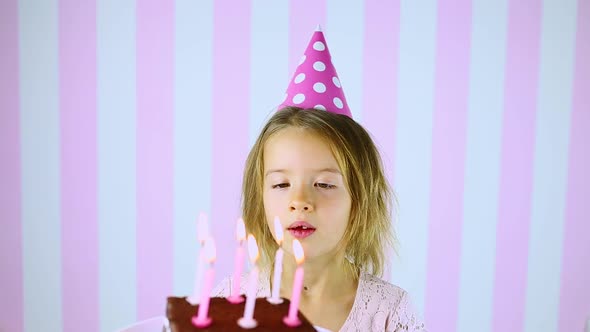 Happy Surprise Close Eyes Little Girl in Pink Cap Blowing Out Candles on a Birthday Cake