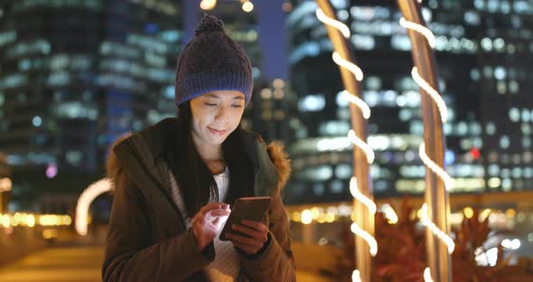 Woman sending sms on smart phone in city at night with city building background