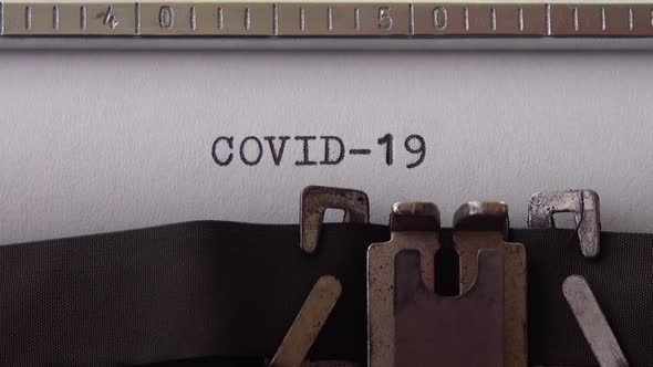 Typing phrase COVID-19 on retro typewriter. Close up.