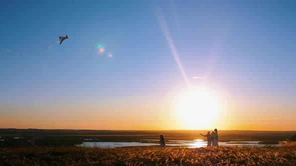 Young Family Playing with a Kite on the Hill - Orange Sunset