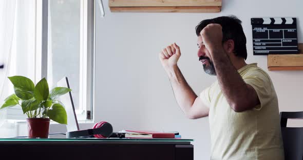 Spanish Bearded Man Celebrating Good News in Front of Laptop at Home