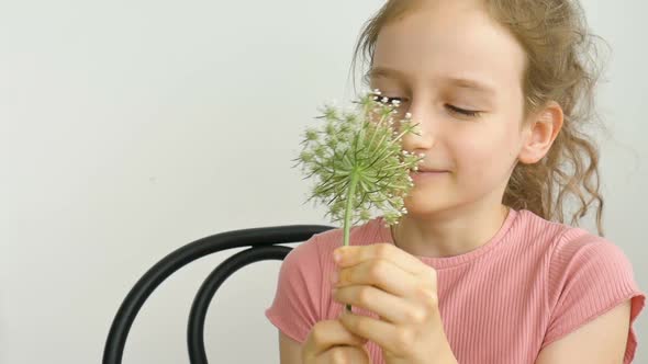Little Girl is Sitting at Home with Flowers in Hands During Summer Time and Sneezing