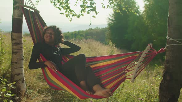 Lovely Smiling Black Woman Hiker in Hammock Enjoying Leisure and Freedom on Mountain Top at Dawn