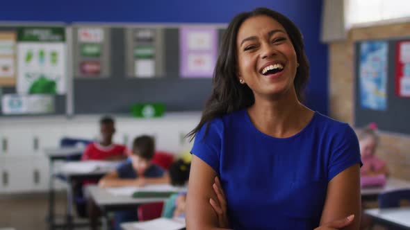 Portrait of happy mixed race female teacher standing in classroom with children in background