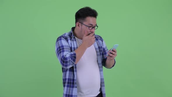 Stressed Young Overweight Asian Hipster Man Using Phone and Getting Bad News