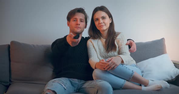 A Young Couple Watching TV, Resting, Hugging, Relaxing. Handsome Man and Attractive Woman Sitting on