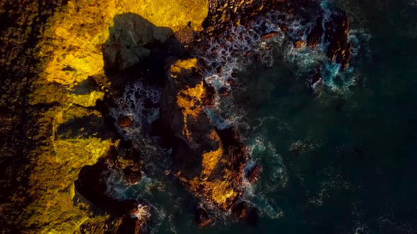 The last sunlight of day illuminates blue ocean waves crashing into rocky cliffs in Big Sur Californ