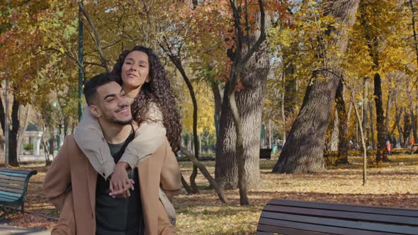 Young Guy Carries Girl on Back Playful Hispanic Couple Walking in Autumn Park Girl Laughing Keep