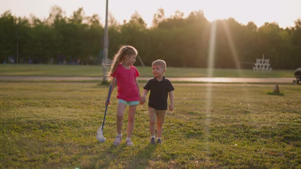 Sister and Little Brother Walk Along Playground at Sunset