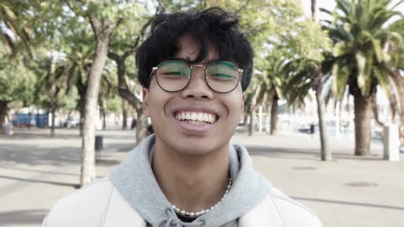 Portrait of Cheerful Young Asian Man Laughing at Camera Outdoors