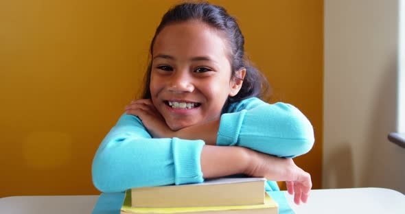 Portrait of smiling girl leaning on stack of books in classroom