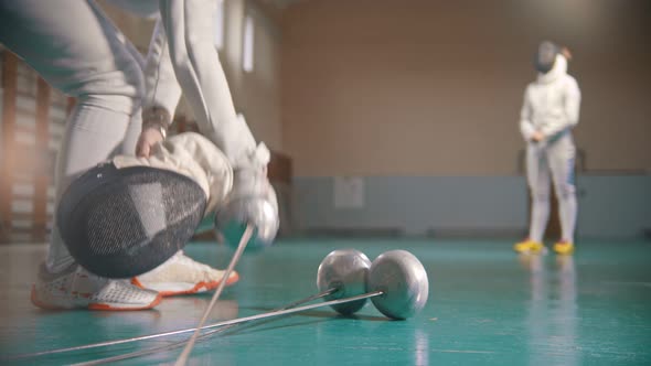 Two Young Women Fencers Having a Training in the Gym - A Woman Takes the Helmet on the Foreground