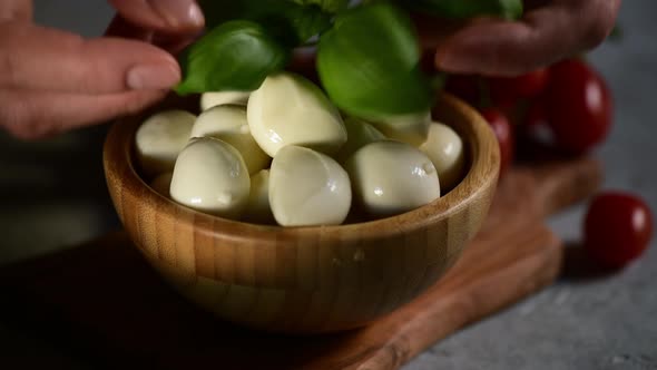 a hand puts the fresh basil leaf on a bowl with mozzarella cheese