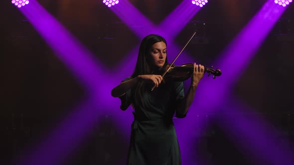 Performance of a Female Violinist on Stage. A Young Brunette Woman Plays the Violin on a Black