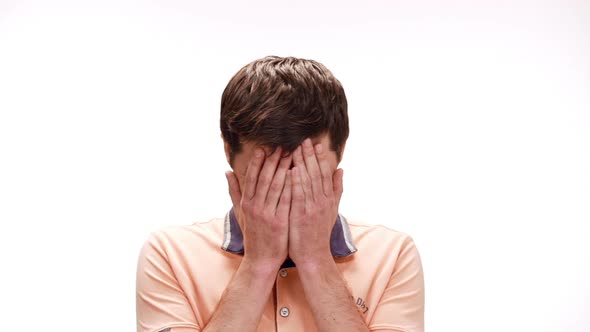 Young Man Smiling Hiding Behind Hands Over White Background Slow Motion