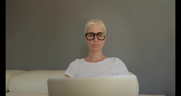 Blonde woman in glasses on sofa with laptop