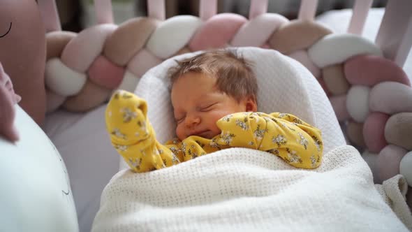 Newborn in a Yellow Jumpsuit Lies in a Retainer of the Child in a Crib