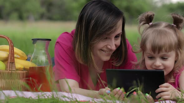 Family Weekend Picnic. Daughter Child Girl with Mother Study Lessons on Tablet. Distance Education