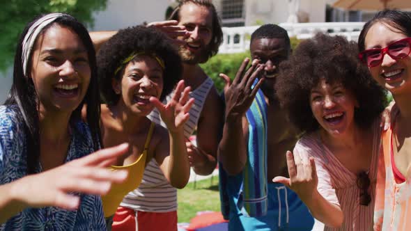 Portrait of diverse group of friends smiling and waving to camera at a pool party