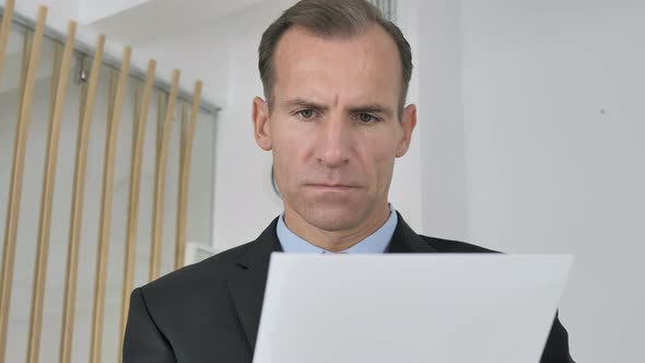 Pensive Middle Aged Businessman Reading Documents in Office, Paperwork