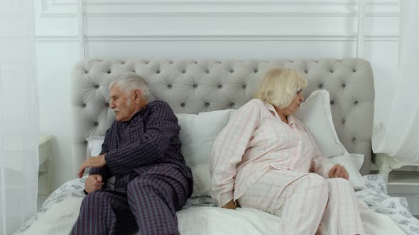Senior Elderly Couple in Pyjamas Lying on Bed Having an Argument in Bedroom, Grandparents Quarrel