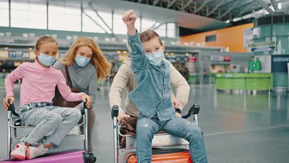 Happy Family of Four Hurrying to Boarding Gates at Airport Building Parents Riding Kids in Luggage