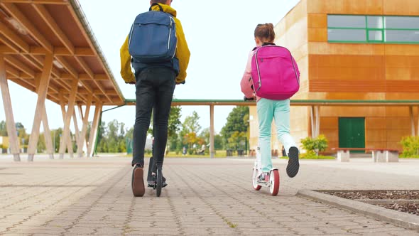 School Children with Backpacks Riding Scooters