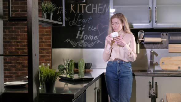 Caucasian woman in home kitchen drinks coffee, opens laptop  checks messages