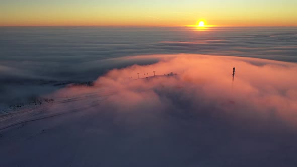 Sunrise above clouds turning them into orange at the top of a ski resort