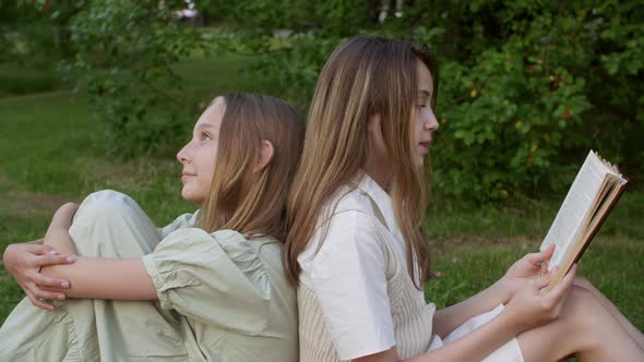 Girls Sitting Together on Grass and Reading Book