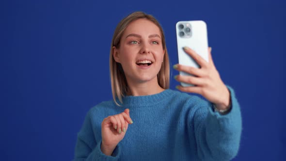 Smiling woman wearing blue sweater talking by video call on phone