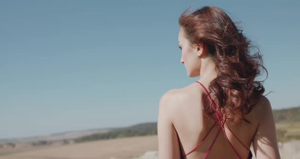 Rear Portrait of Elegant Lady with Naked Shoulders Stands Among Desert