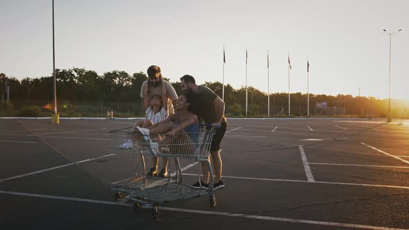 Young Girls and Guys are Racing on Shopping Carts at Deserted Parking Lot