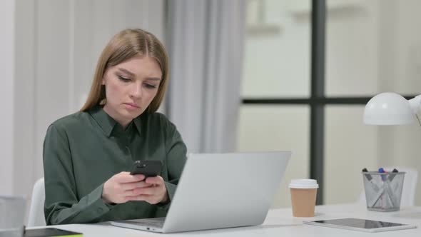 Young Woman Using Smartphone While Working on Laptop